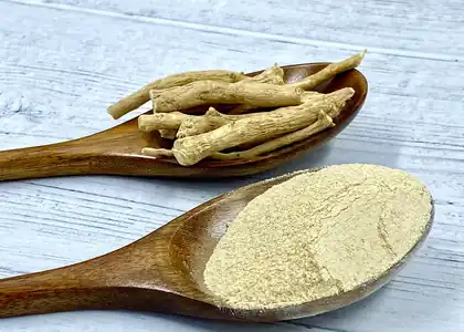 Корень ашваганды, порошок и чашка тёплого молока с мёдом на деревянном столе