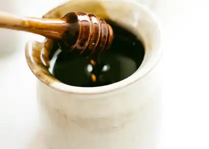 Деревянная ложка с мёдом, банка с сотами и чашка травяного чая на фоне русской печи